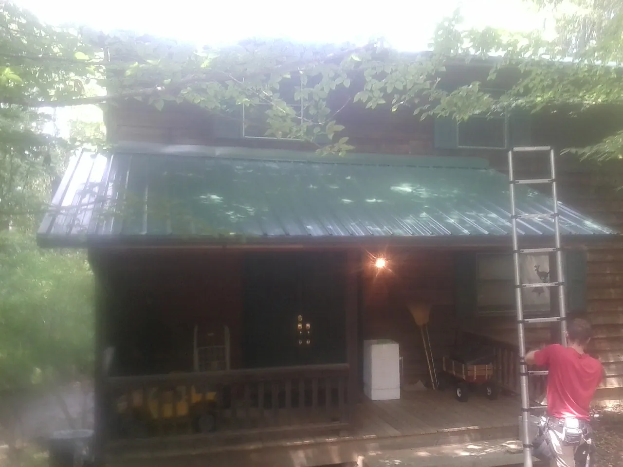 Worker on a ladder at the green porch roof of a wooded cabin in Sheridan